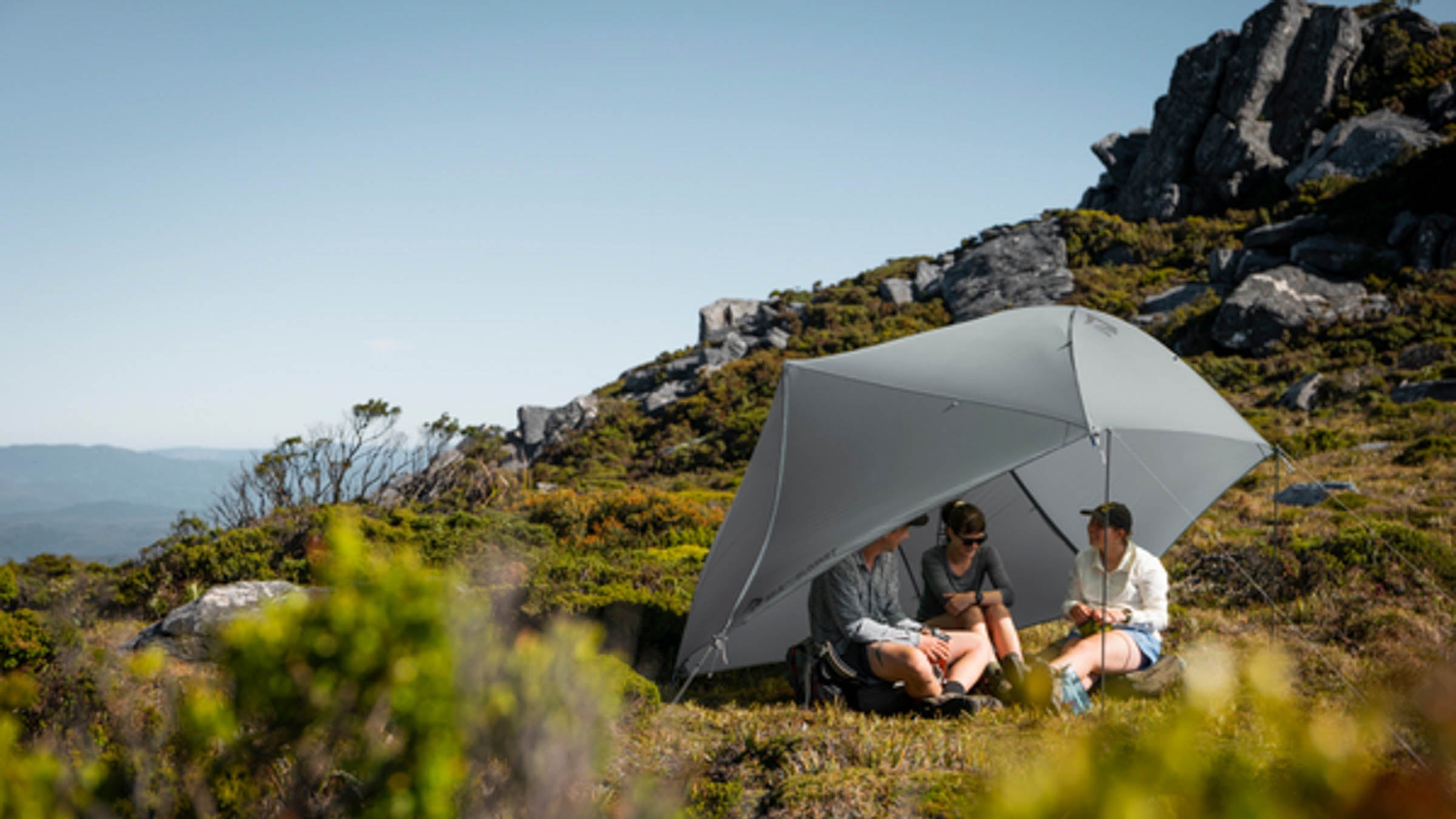 Three people sitting under shade in the wilderness