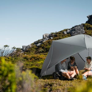 Three people sitting under shade in the wilderness