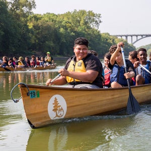 A group of kids paddling a wooden canoe in Thrive Outside program