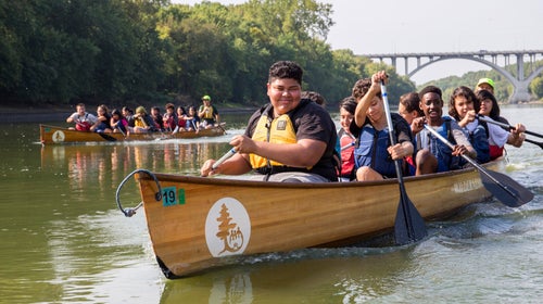 A group of kids paddling a wooden canoe in Thrive Outside program