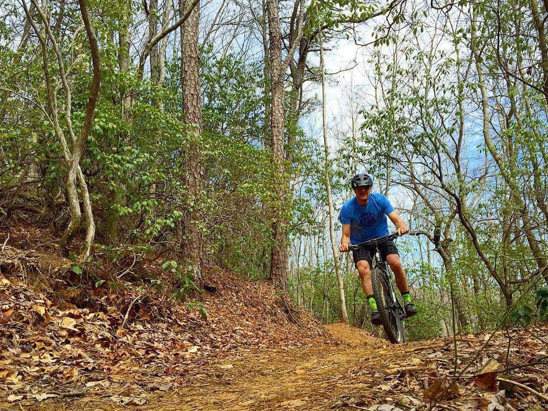 Man in blue shirt mountain biking down wooded trail