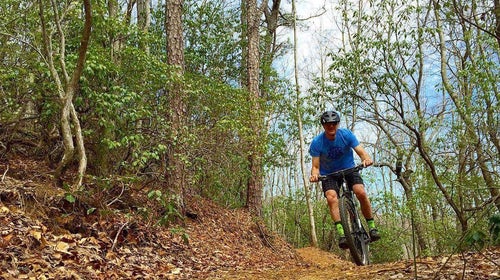 Man in blue shirt mountain biking down wooded trail