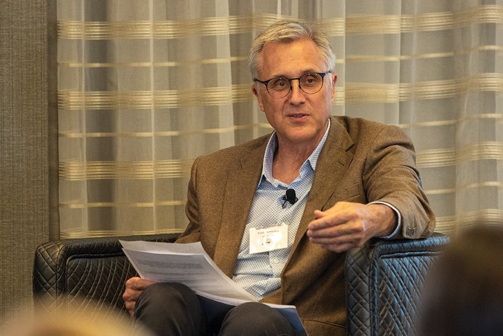 Man wearing brown blazer, blue button down shirt and glasses sitting in chair holding paper | Tom Dempsey infrastructure