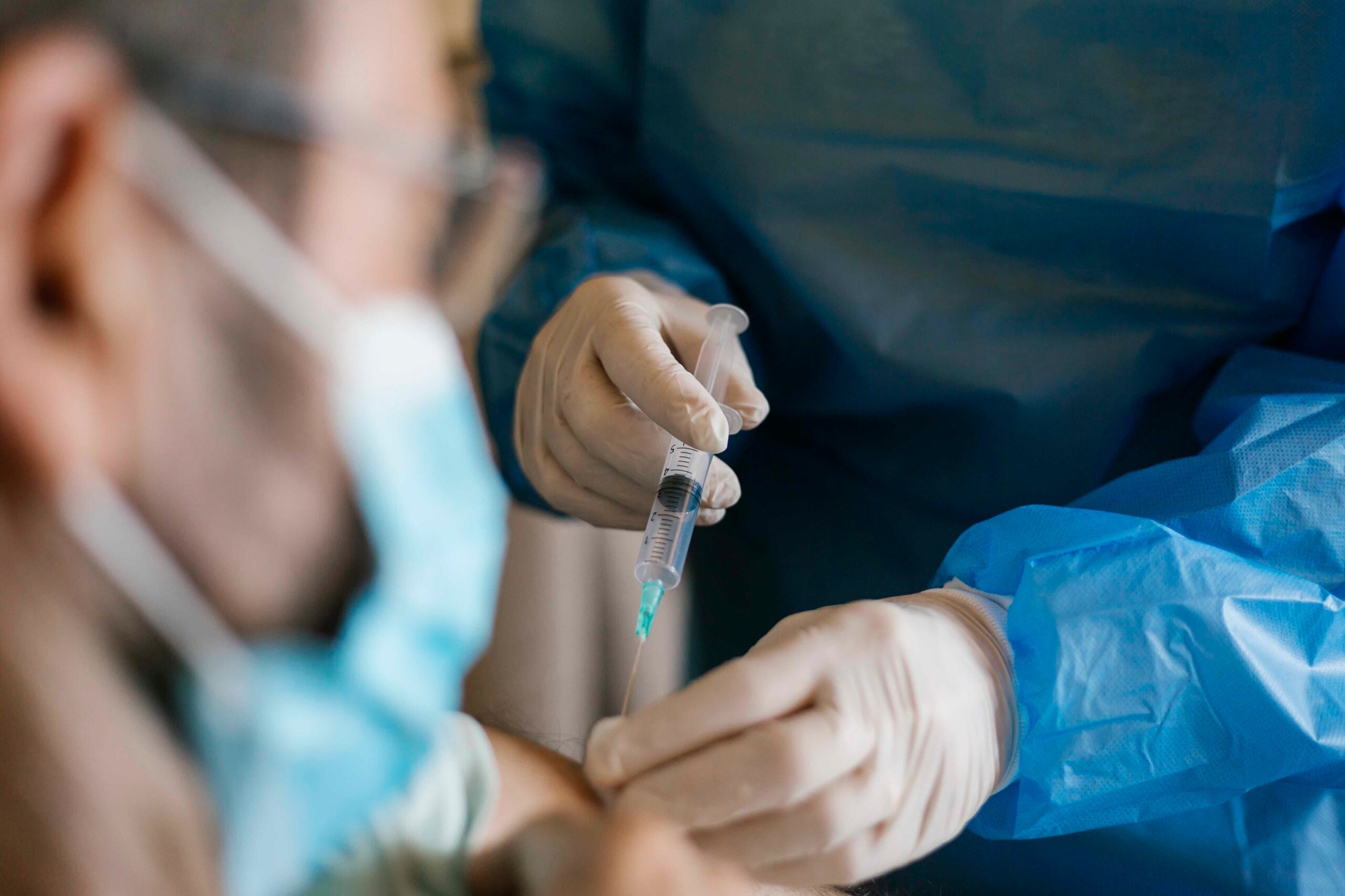 Doctor injecting covid-19 vaccine to senior man at his home.