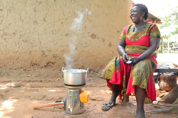 Kenyan woman in red and gold dress boiling water and charging her mobile phone with a BioLite HomeStove.