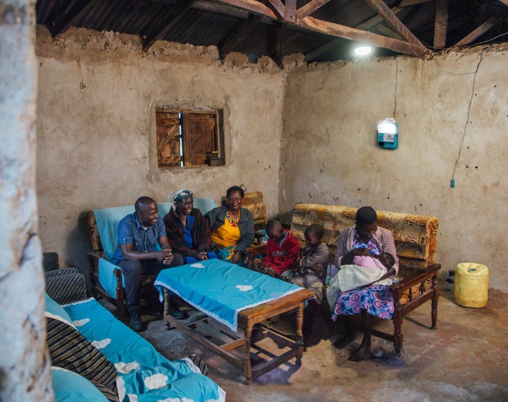 Biolite lighting illuminates a concrete home in Africa, where a family gathers around a table.