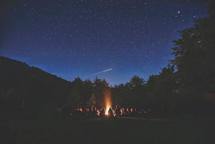People gathered around a campfire at night | The Oath