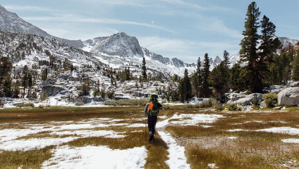 Woman backpacking through the Eastern Sierras in California with snow on the mountains behind her