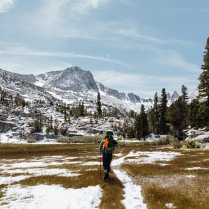 Woman backpacking through the Eastern Sierras in California with snow on the mountains behind her