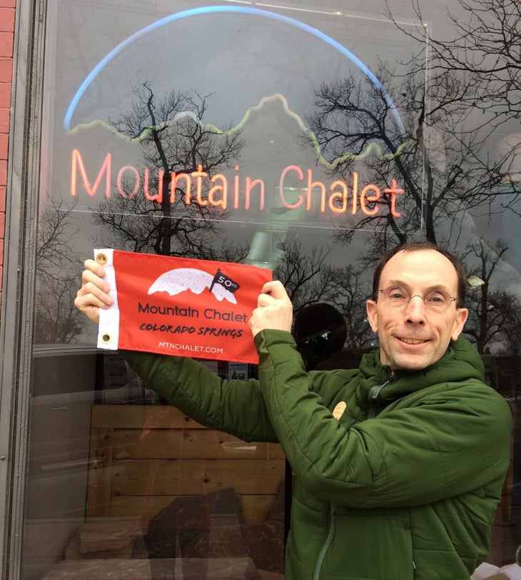 Jim Smith holds up a 50th anniversary flag for Mountain Chalet in Colorado Springs