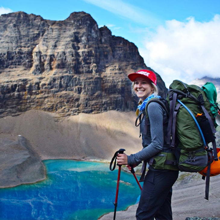 Courtney Crowe 1 Instagram influencer Courtney Crowe stands with a green backpack and trekking poles with small turquoise apline Lake Oesa in the background.