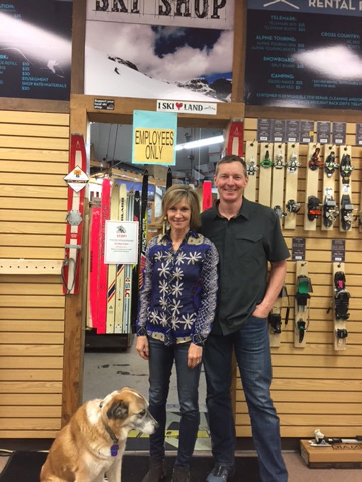 A man and woman with a dog in retail store with ski bindings and employee entrance on back wall.  Neptune Mountaineering