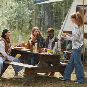 Full length view at diverse group of friends enjoying picnic outdoors at campsite with trailer van