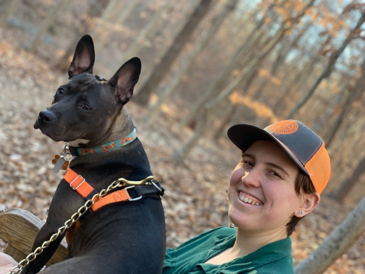 Emmy Johnson wearing green shirt and orange and gray hat with dog in the woods