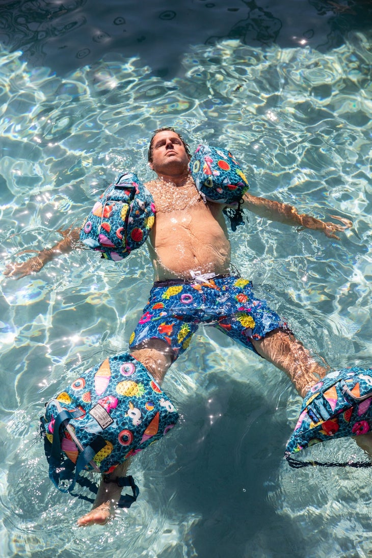KAVU lifestyle clothing | Man floating in pool with colorful swim trunks and accessories