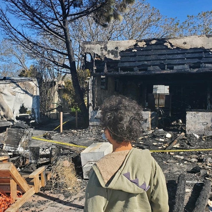 A person in a green hoodie stands in front of the burned out wreckage of a building, Montezuma Valley Market fire