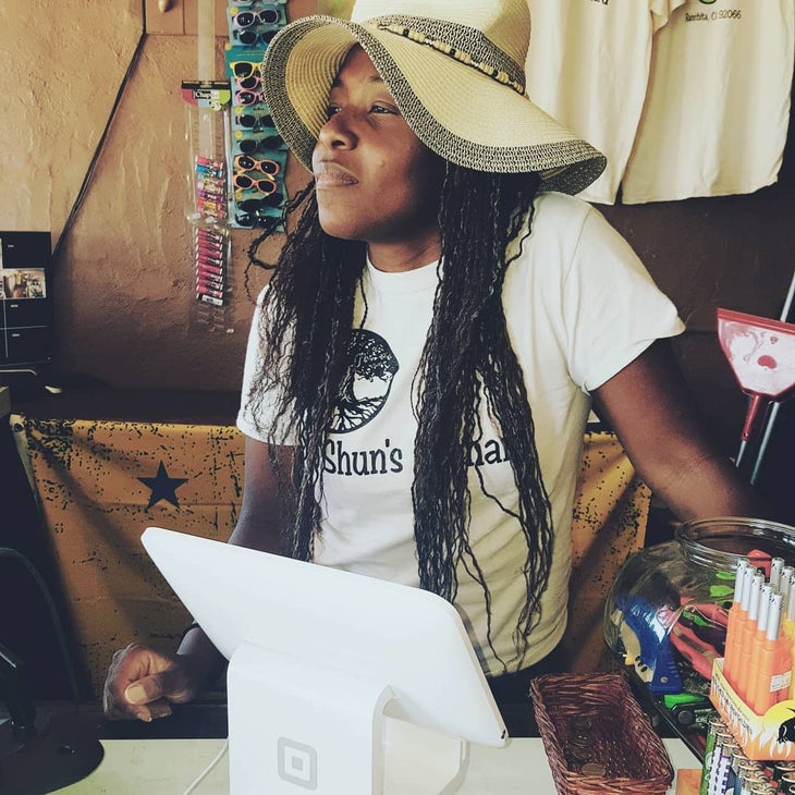 Black woman with long black hair and floppy sun hat stands in front of a cash register looking off to the side | Montezuma Valley Market fire