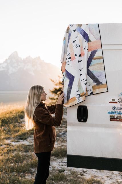 Nomas Wylder towel collab | patterned towel hanging off the back of a white van with long-haired blond woman touching it