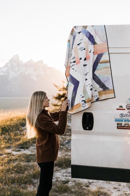 Nomad-Wylder-Towel-collab Nomas Wylder towel collab | patterned towel hanging off the back of a white van with long-haired blond woman touching it