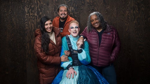 four people posing in front of brown background