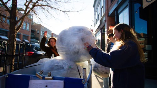 Woman placing bag into blue bin in front of a shop
