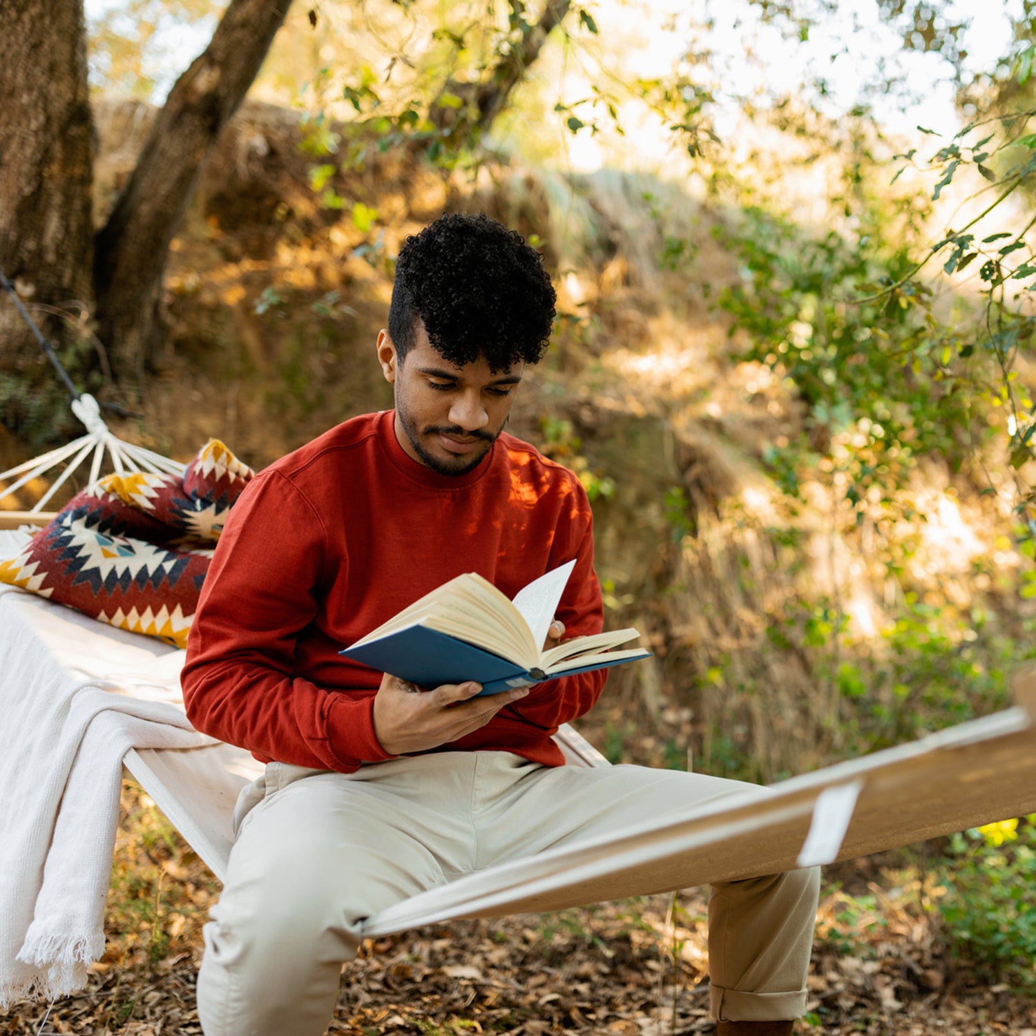 Young man sitting in a hammock reading a book while enjoying nature