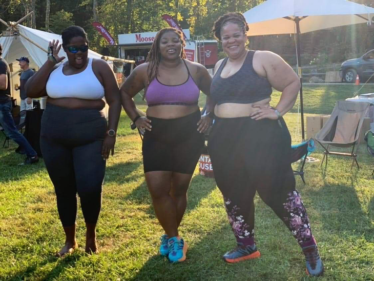 Mirna Valerio, Latoya Shauntay, and Latria Graham, smile as they stand in their sports bras and leggings at the Pursuit Series.