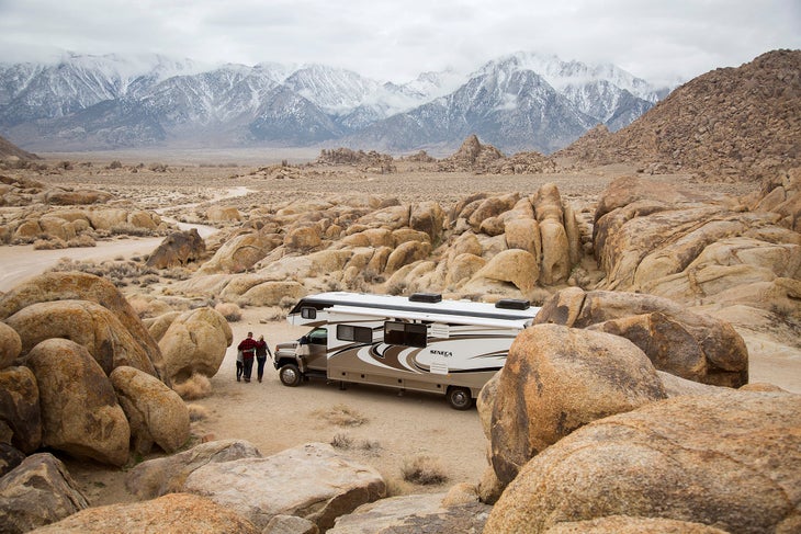 Large RV parked in the desert with snow-covered mountains in background and a family enjoying the view