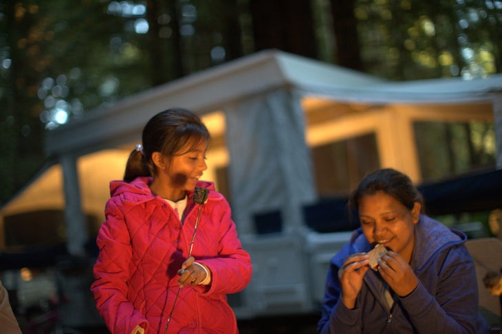 A woman and her daughter eating s'mores in front of an RV camper
