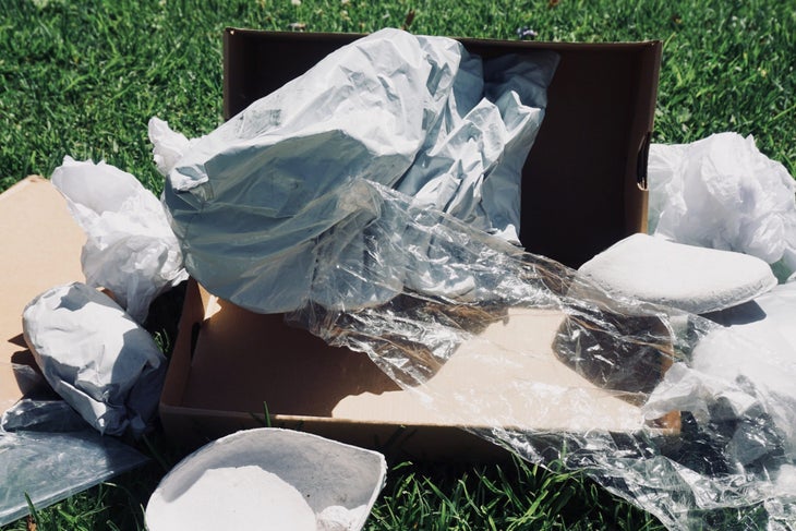 A pile of paper, plastic, and cardboard litter the grass in a display of wasteful packaging that is not sustainable.