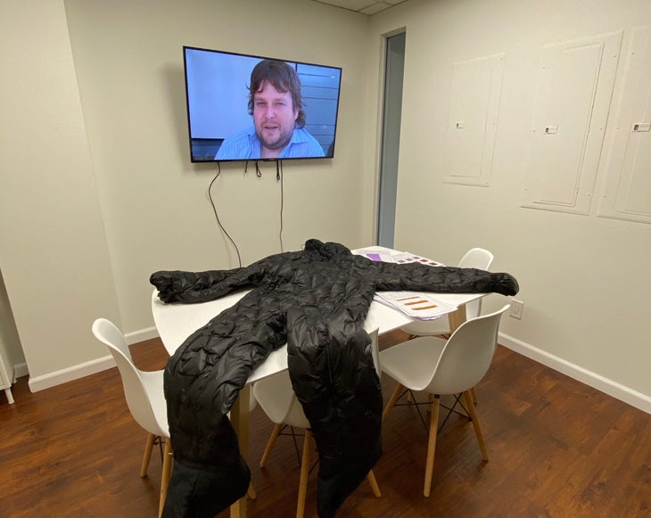"a man on a tv screen in a white room with a puffy snowsuit lying on a table"
