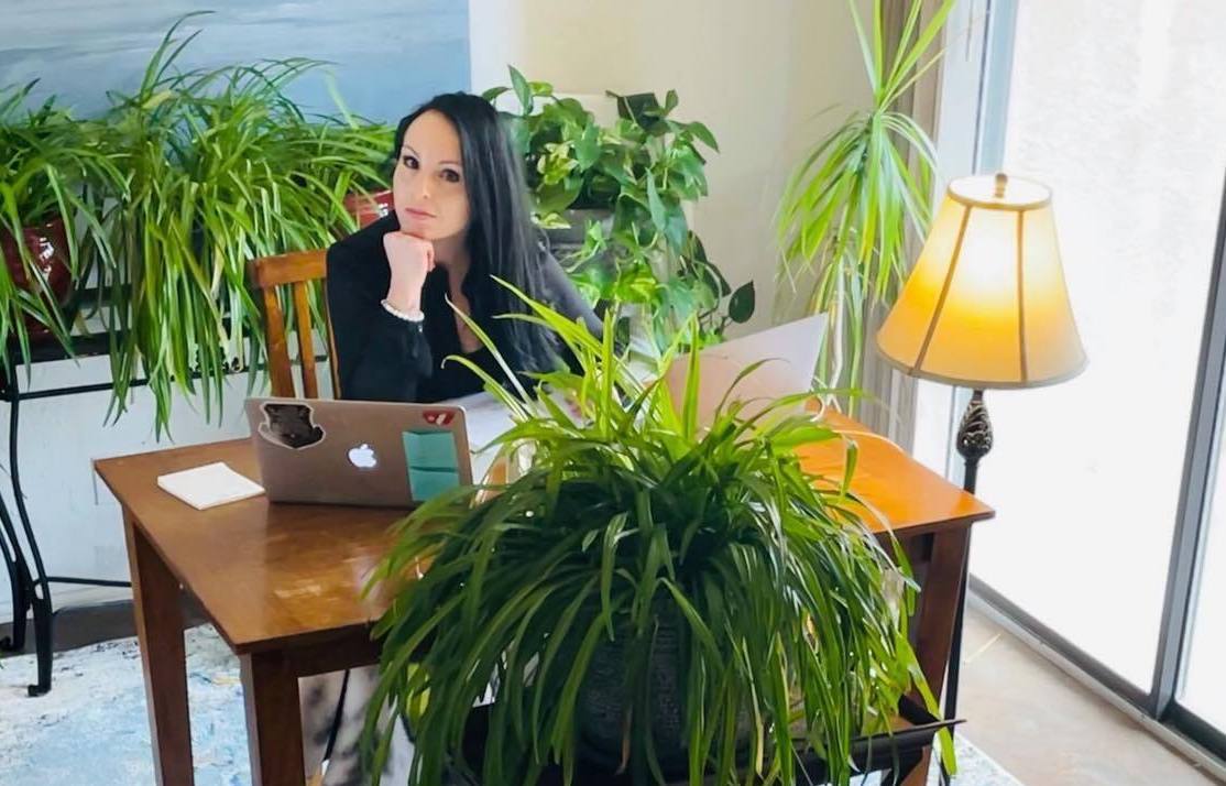 woman with long dark hair, Stephanie Maez from Outdoor Foundation, sitting at desk with green plants around her