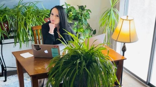 woman with long dark hair, Stephanie Maez from Outdoor Foundation, sitting at desk with green plants around her