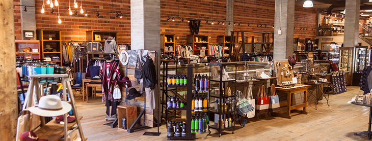 A retail shop with warm wood walls and floots, racks with hats, water bottles, bags and more