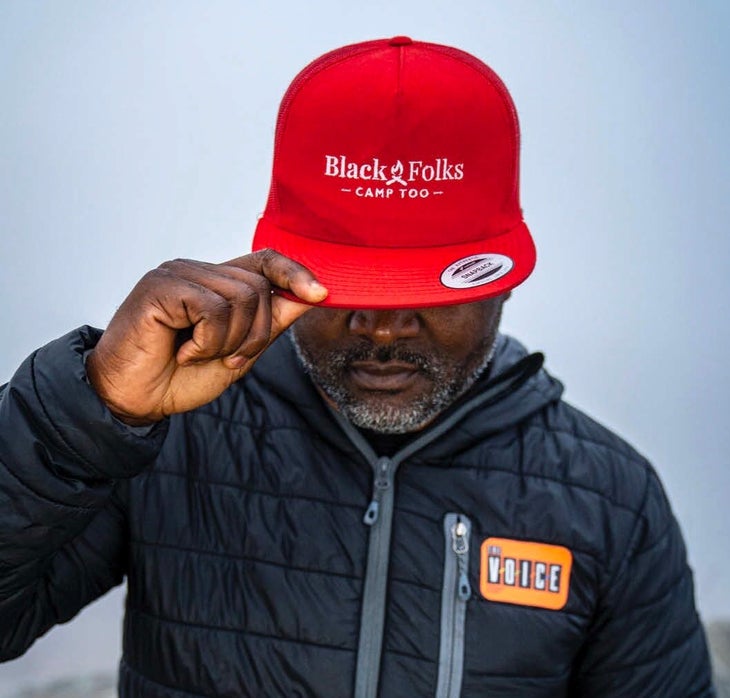 "Man with a red hat looks down and holds the brim"