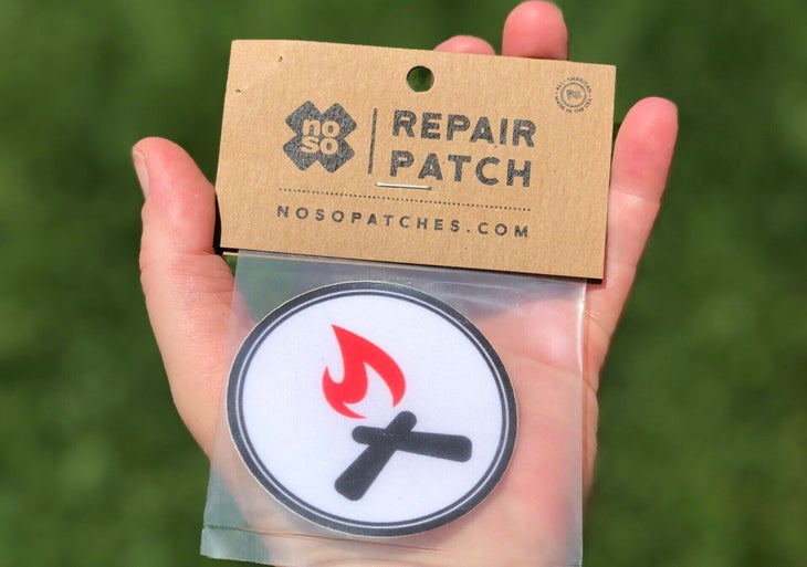 hand holding a Noso patch featuring a campfire logo