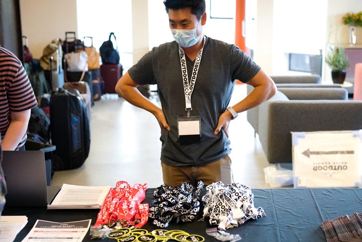 Yoon Kim stands at registration desk of Outdoor Media Summit with lanyards and stickers on the table
