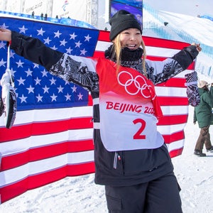 Chloe Kim smiles and holds a US flag in front of ski slopes in Zhangjiakou, China.