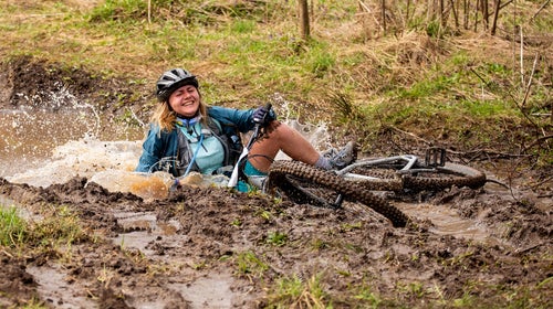A woman crashes into mud on her bicycle.