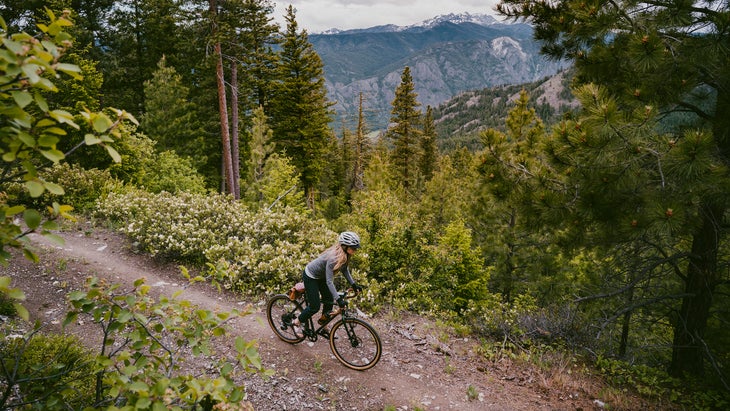 Woman bikes on rocky ridge trail overlooking mountain valley