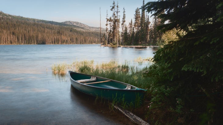 Lone dark green canoe surrounded by ultra-smooth water from long exposure on shores of Upper Payette Lake outside McCall, Idaho