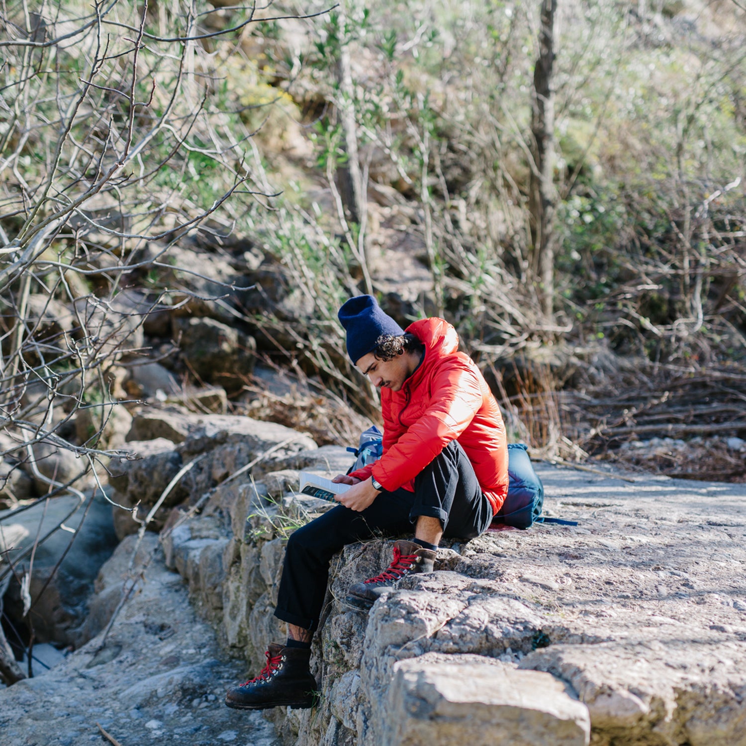 Young man sitting with book on the cliff. Horizontal outdoors shot.