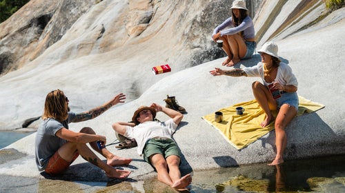 Several people enjoy a summer day on rocks by a river. One tosses a can of Stillhouse whiskey to another.