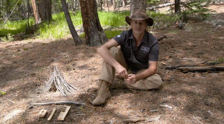 Shane Hobel sits on the forest floor with fire-building materials.