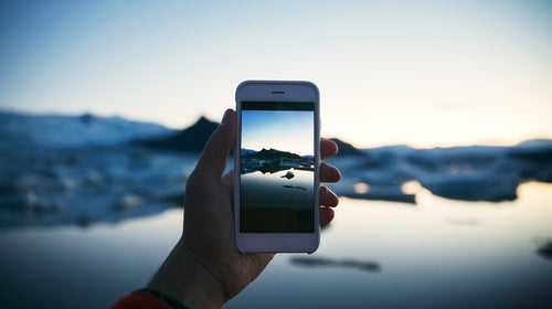 Cropped hand photographing lake through smart phone during winter