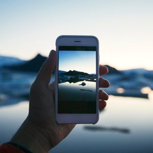 Cropped hand photographing lake through smart phone during winter