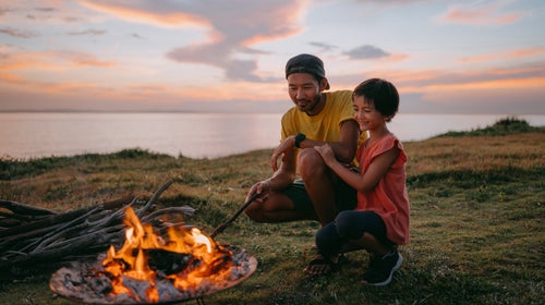 Father and daughter enjoying campfire at campsite at sunset