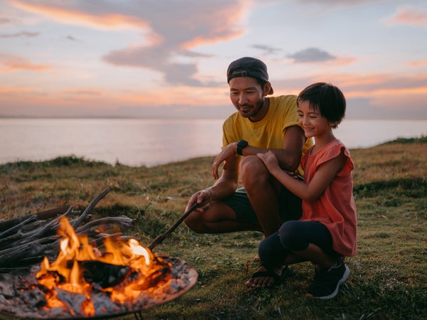Father and daughter enjoying campfire at campsite at sunset
