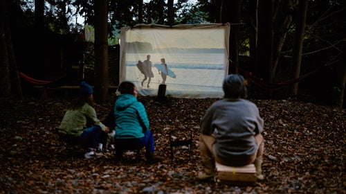 People watching outdoor movies in front of wooden camp hut