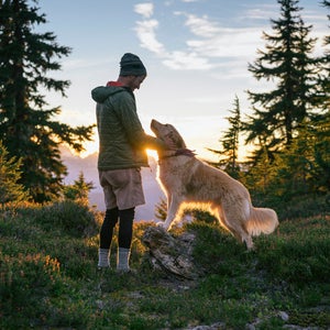 A hiker pets his dog at sunset in the mountains.
